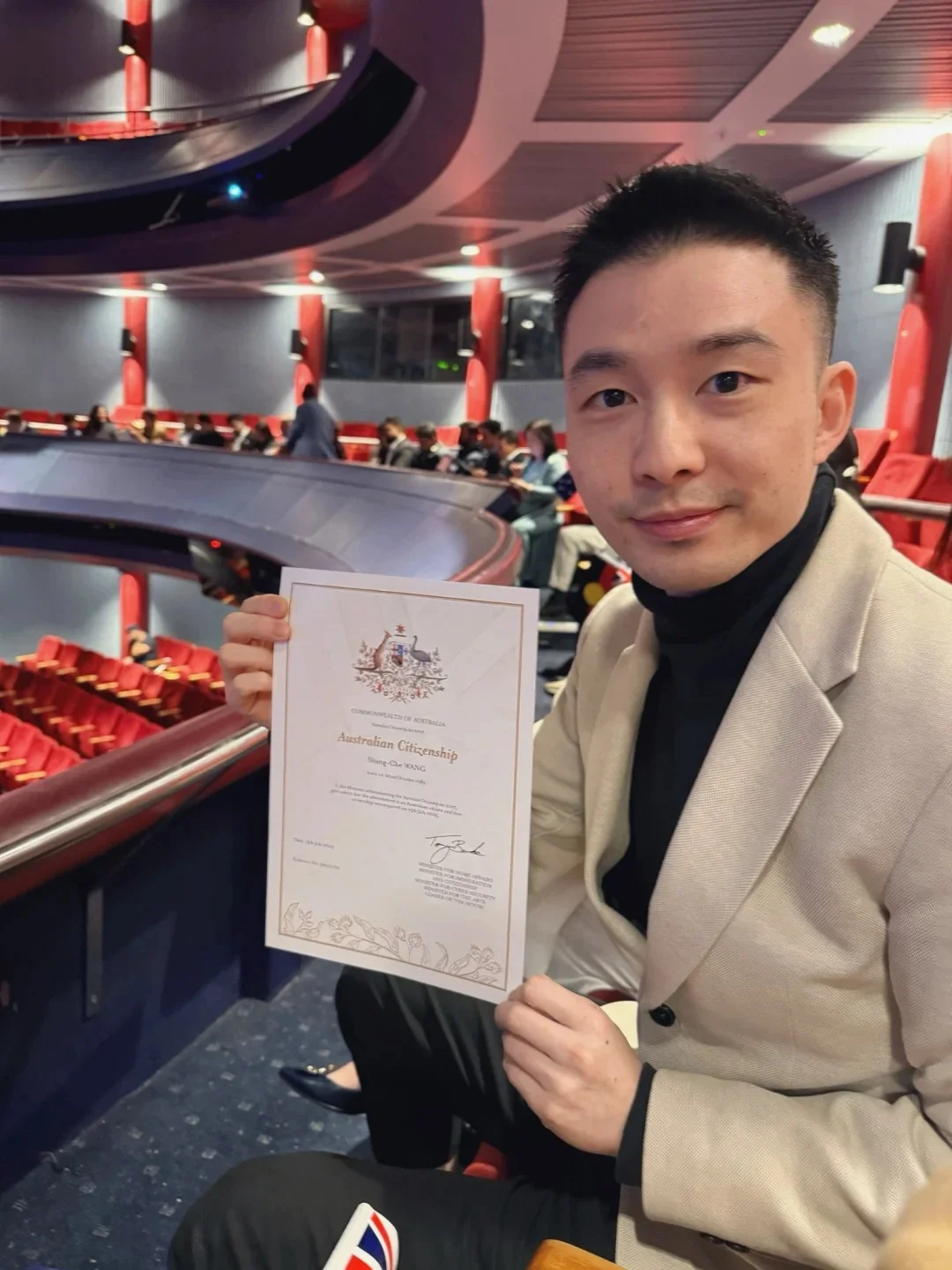 Man holding Australian citizenship certificate at ceremony venue
